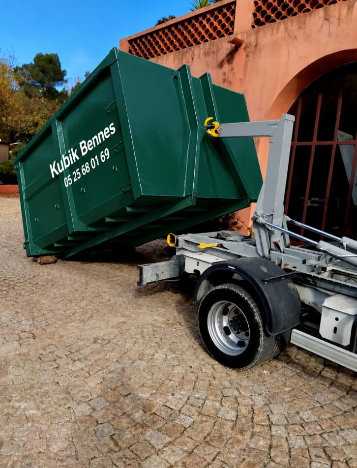 Benne verte Kubik Bennes déposée dans une cour pavée devant une maison